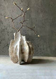 a white vase with branches in it on top of a gray table next to a wall