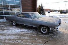 an old car is parked in front of a building with snow on the ground around it