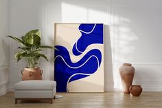 a blue and white abstract painting in a living room with a chair, potted plant and vases on the floor