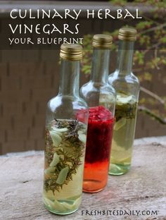 three bottles filled with different colored liquids and herbs on top of a wooden table