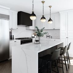 a kitchen with white cabinets and marble counter tops, black appliances and pendant lights hanging from the ceiling