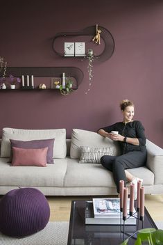 a woman sitting on top of a couch in a living room next to a purple wall