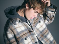 a young man in a plaid coat is holding his hands to his head and looking down