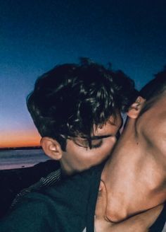 two young men are kissing each other on the beach at night, while the sun is setting