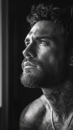 a black and white photo of a man with tattoos on his chest, looking off into the distance