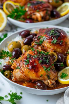 two white bowls filled with chicken and olives next to lemon wedges on top of rice