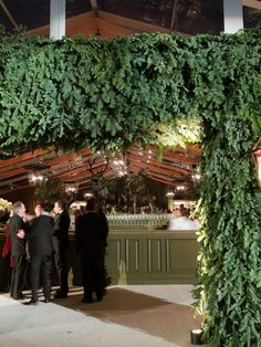 people are standing under an arch covered with greenery at a wedding reception in the evening