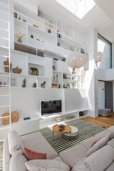 a living room filled with lots of white furniture and bookshelves on the wall