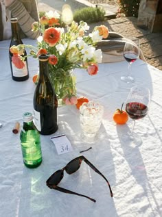 the table is set with glasses, bottles and flowers in vases on top of it