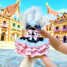 a hand is holding a doll in front of a building with pink and white ruffles