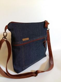 a denim purse with brown leather straps on a white background, showing the front pocket and shoulder strap