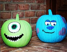 two pumpkins painted to look like monsters sitting next to each other in front of a brick wall