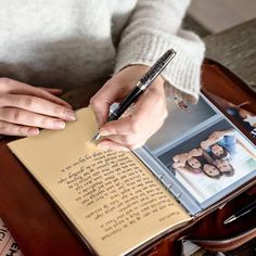 a person writing on a book with a pen in their hand while sitting at a table