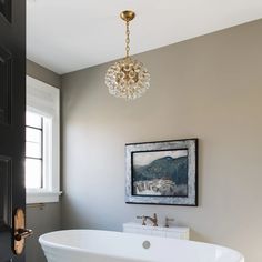 a white bath tub sitting under a chandelier next to a painting on the wall