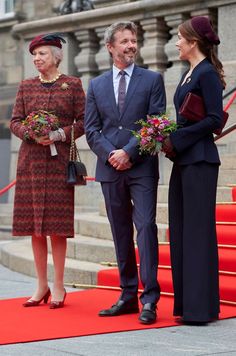 two women and a man are standing on a red carpet in front of some stairs