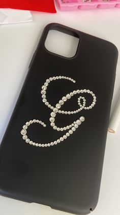 a black phone case with the letter g on it and some beads attached to it