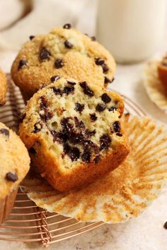 muffins with chocolate chips sitting on top of a wire rack next to a glass of milk