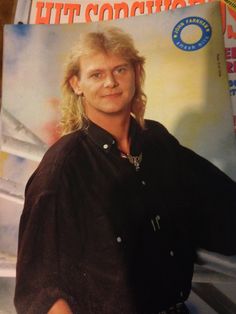 a man with long hair standing in front of a magazine