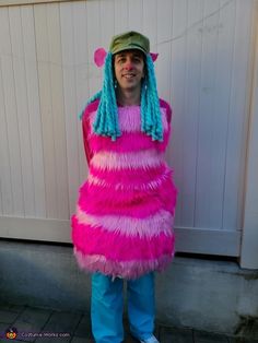 a person wearing a pink and blue costume standing in front of a white wall with a green hat on