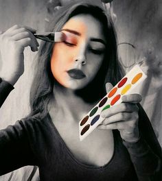 a woman is holding a palette and painting her face