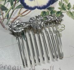 This is a unique handmade small, silver hair accessory, up cycled from a sterling silver floral brooch. This pre owned up cycled sterling silver hair comb features a small sprig of flowers in an Art Nouveau style. The perfect bridal hair accessory for a vintage inspired wedding.  The reverse is fully hallmarked London 1990.  The brooch pin is still intact and has been wired onto the hair comb, so that you could remove and wear again as a brooch if you wish.  As a  preloved, piece will show slight signs of wear relative to its age.  Approximate measurements  Length 5 cm Brooch Length 5 cm  Total comb height 4 cm This item will arrive in a gift box.  Postage will be combined for purchases made in the same transaction. Silver Hair Accessory, Floral Hair Comb, Silver Hair Comb, Theme Vintage, Floral Hair Combs, Floral Accessories Hair, Flower Hair Comb, Vintage Inspired Wedding, Bridal Hair Comb