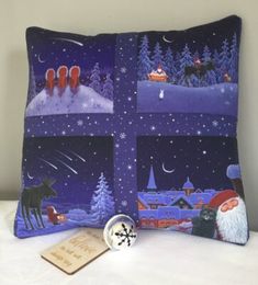 a decorative pillow with pictures of santa and his reindeers in the night sky, sitting on a bed