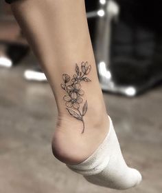 a woman's foot with a small flower tattoo on the left side of her ankle