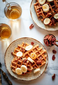 two plates with waffles, bananas and pecans next to glasses of beer