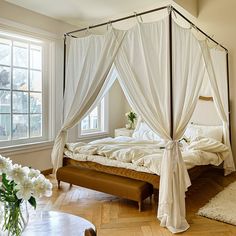 a white canopy bed sitting in a bedroom next to a table with flowers on it