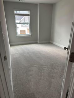 an empty room with carpeted flooring and a window in the corner is shown