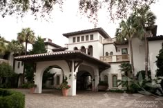 a large white building with palm trees and potted plants on the front porch area