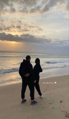 two people standing on the beach looking out at the water and clouds in the sky