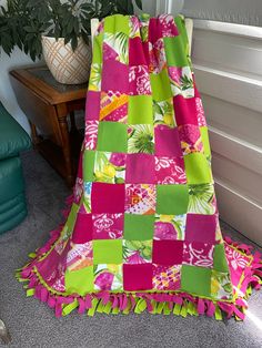 a pink and green blanket sitting on top of a floor next to a potted plant