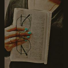 a woman holding an open book with glasses on it