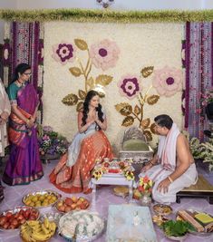 a man and woman sitting in front of a cake on a table surrounded by other people