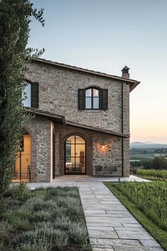 a stone house with black shutters on the windows and doors is shown in front of an olive tree