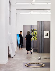 two women looking at art on display in an open space with white walls and floors