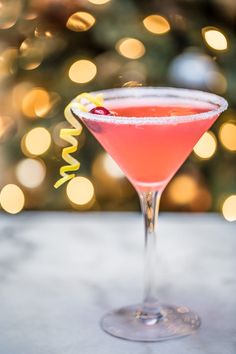 a pink cocktail in a martini glass with a christmas tree in the background