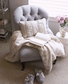 a chair with a book and slippers on it next to a vase filled with flowers