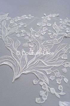 an embroidered fabric with white flowers and leaves on grey background, suitable for use in wedding gowns