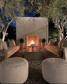 an outdoor fireplace with wicker furniture and potted trees in the background at night