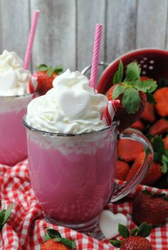 two mugs filled with whipped cream and strawberries on a checkered tablecloth