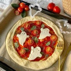 a pizza topped with tomatoes and cheese on top of a table next to utensils