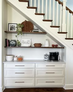 a kitchen under the stairs with white cabinets and drawers underneath it, along with a coffee maker