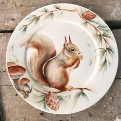 a plate with a painting of a squirrel on it's side and pine cones in the background