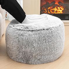 a person standing on top of a fluffy gray bean bag chair next to a fire place