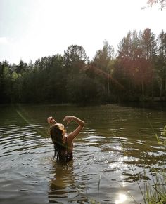 a woman is standing in the water with her hands behind her head and arms above her head