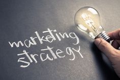 a hand writing the word marketing strategy on a chalkboard with a lightbulb