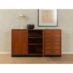 a wooden cabinet sitting on top of a hard wood floor next to a painting and lamp