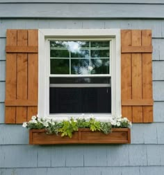 an open window with wooden shutters and white flowers in the windowsill on a blue house